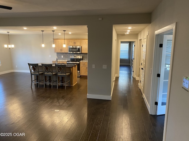 kitchen featuring light brown cabinetry, decorative light fixtures, a center island with sink, stainless steel appliances, and decorative backsplash