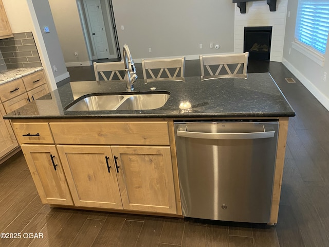 kitchen featuring a kitchen island with sink, sink, stainless steel dishwasher, and dark stone counters