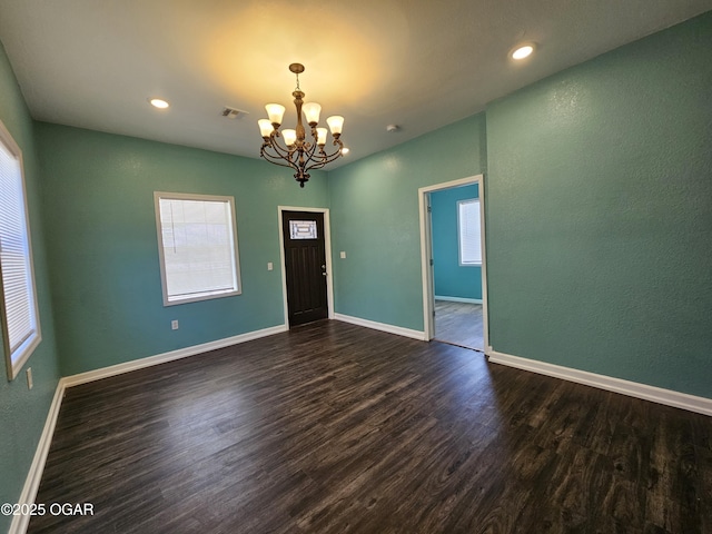 empty room featuring an inviting chandelier and dark hardwood / wood-style flooring