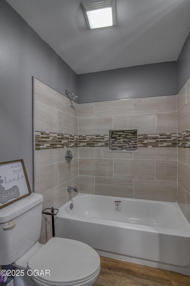 bathroom featuring hardwood / wood-style floors, tiled shower / bath, toilet, and a textured ceiling