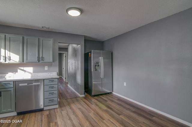 kitchen featuring hardwood / wood-style flooring, stainless steel appliances, gray cabinets, and a textured ceiling