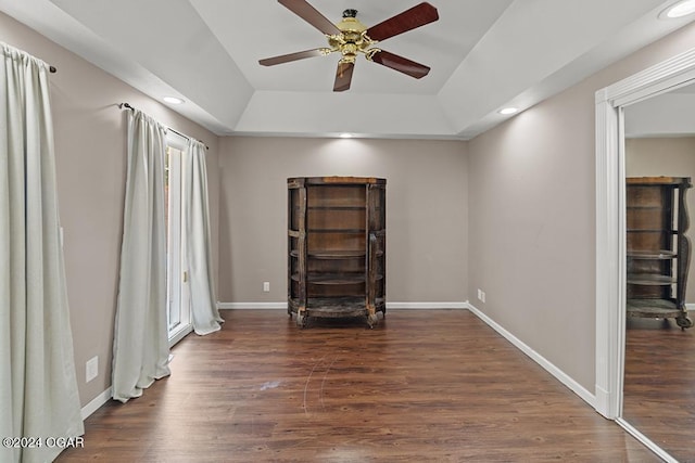 unfurnished bedroom with ceiling fan, a tray ceiling, and dark hardwood / wood-style flooring