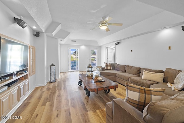 living room featuring light hardwood / wood-style floors, a raised ceiling, and ceiling fan