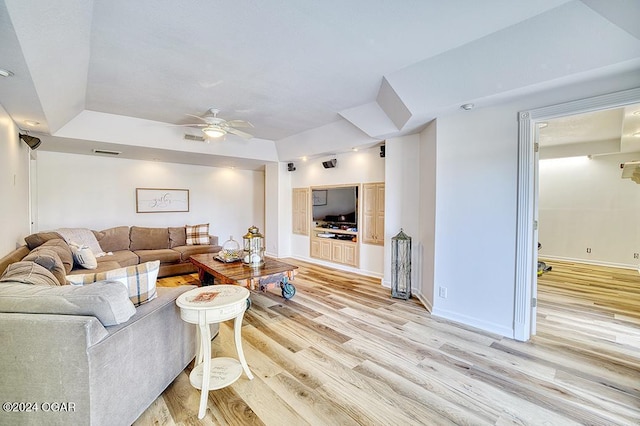 living room featuring ceiling fan, a tray ceiling, and light wood-type flooring