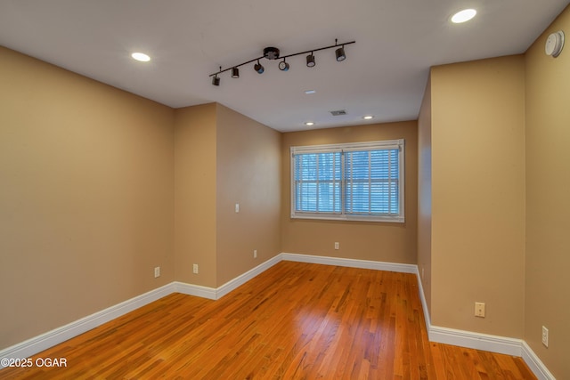 empty room with track lighting and light hardwood / wood-style floors