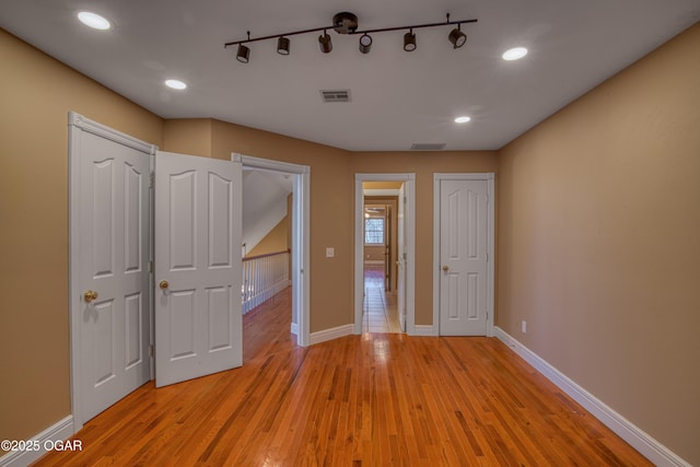 unfurnished bedroom with light hardwood / wood-style floors and rail lighting