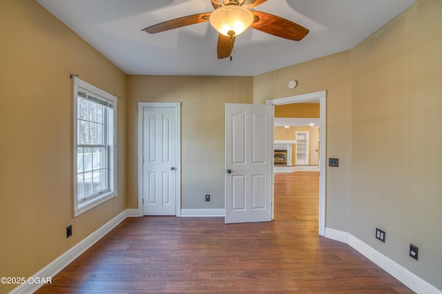 unfurnished bedroom featuring a tile fireplace, dark wood-type flooring, ceiling fan, and a closet