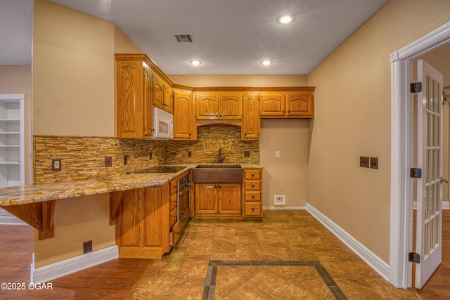 kitchen with a breakfast bar, sink, light stone counters, black electric cooktop, and kitchen peninsula