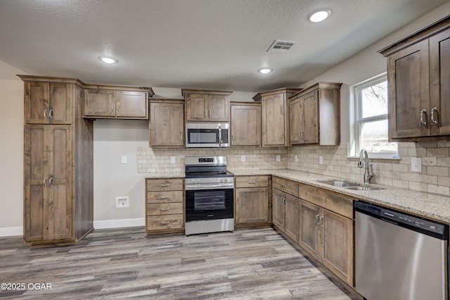 kitchen featuring sink, light wood-type flooring, stainless steel appliances, and light stone countertops