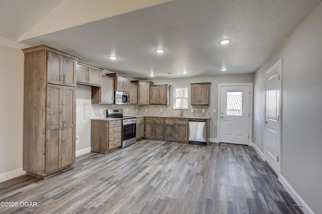 kitchen featuring vaulted ceiling, appliances with stainless steel finishes, tasteful backsplash, sink, and light hardwood / wood-style floors