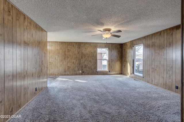 spare room featuring a textured ceiling, wooden walls, ceiling fan, and carpet flooring