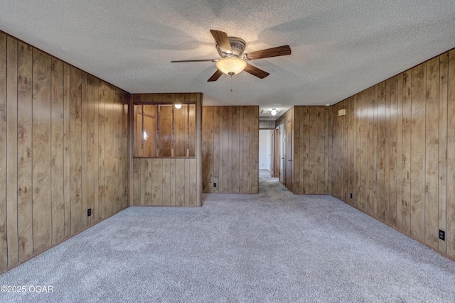 carpeted empty room featuring ceiling fan, a textured ceiling, and wood walls