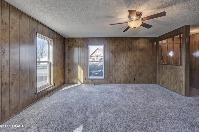 carpeted empty room featuring wooden walls and a textured ceiling