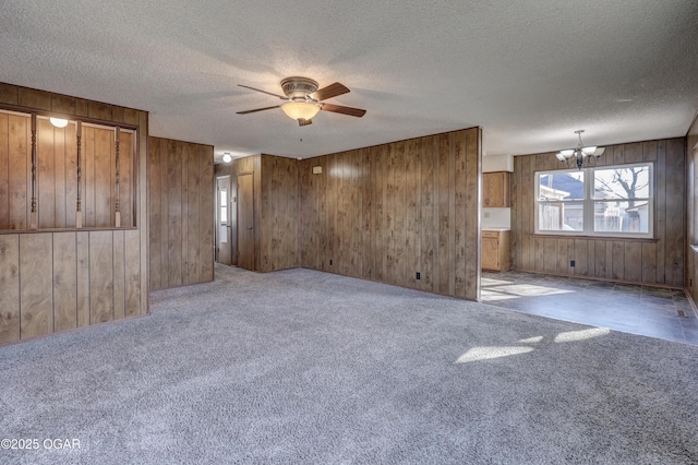 carpeted empty room featuring ceiling fan with notable chandelier, a textured ceiling, and wood walls