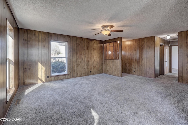 carpeted spare room featuring a textured ceiling, ceiling fan, and wood walls