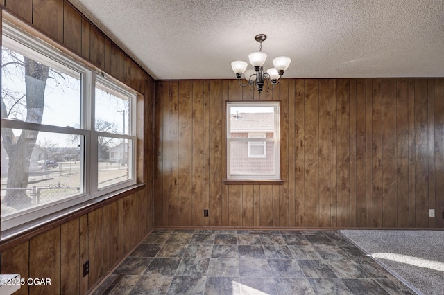 unfurnished room featuring a notable chandelier, wooden walls, and a textured ceiling