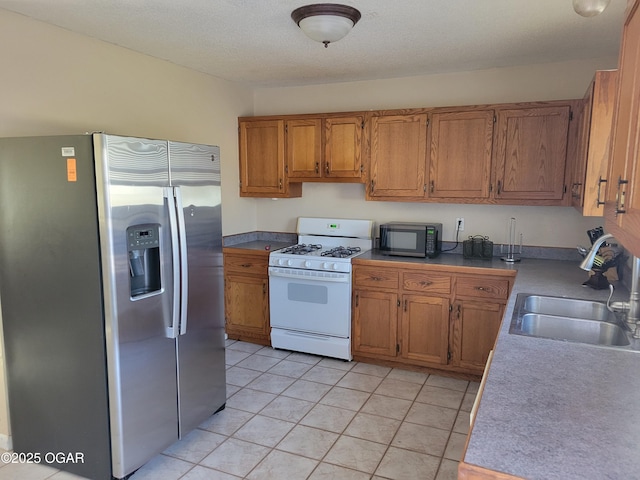 kitchen with white gas range, sink, light tile patterned floors, stainless steel fridge with ice dispenser, and a textured ceiling