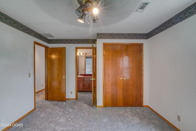 unfurnished bedroom with ceiling fan, ensuite bath, light colored carpet, and a textured ceiling