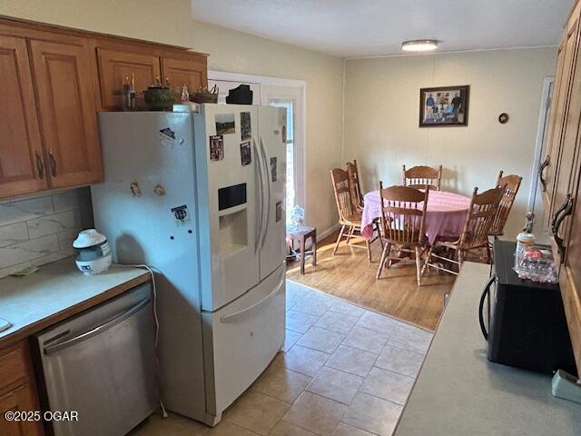 kitchen with dishwasher, white refrigerator with ice dispenser, light tile patterned floors, and backsplash