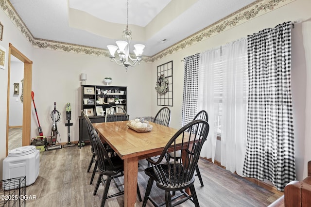 dining area featuring a notable chandelier, a tray ceiling, and wood-type flooring