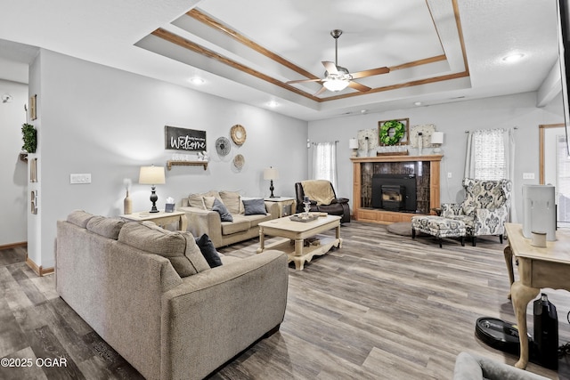 living room featuring a tile fireplace, ceiling fan, hardwood / wood-style floors, ornamental molding, and a raised ceiling