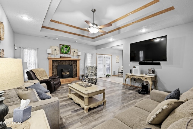 living room with light wood-type flooring, ornamental molding, ceiling fan, a tray ceiling, and a textured ceiling