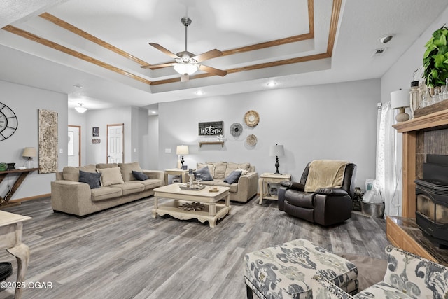 living room featuring ceiling fan, a raised ceiling, light hardwood / wood-style floors, and a wood stove