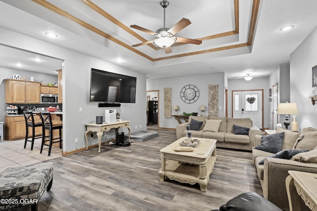 living room featuring light hardwood / wood-style flooring, ornamental molding, a raised ceiling, and ceiling fan