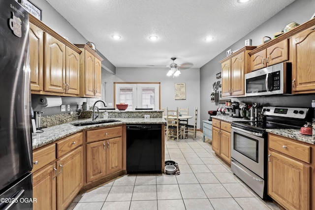 kitchen with appliances with stainless steel finishes, sink, light tile patterned floors, light stone counters, and a textured ceiling