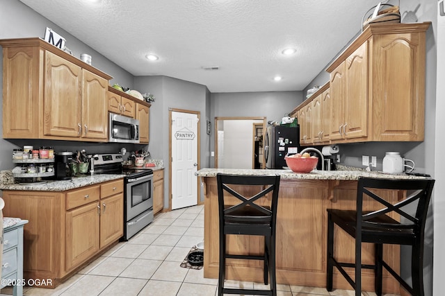 kitchen with stainless steel appliances, a kitchen bar, light stone countertops, and light tile patterned floors