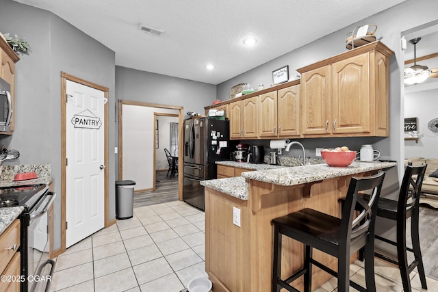 kitchen with light tile patterned floors, range with electric cooktop, a kitchen breakfast bar, light stone counters, and black fridge with ice dispenser