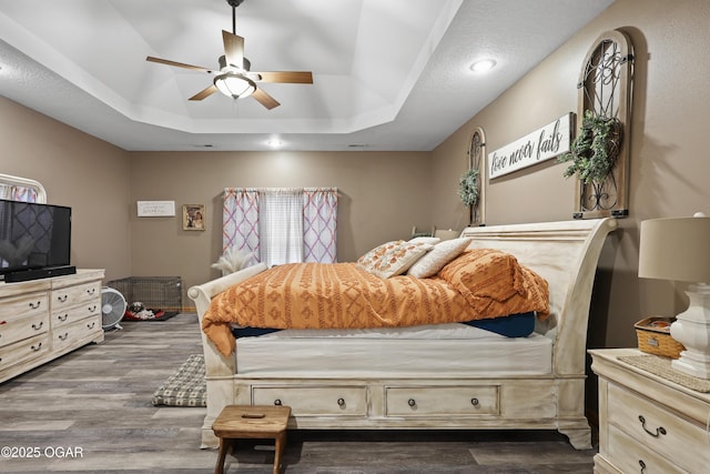 bedroom with dark wood-type flooring, ceiling fan, and a raised ceiling