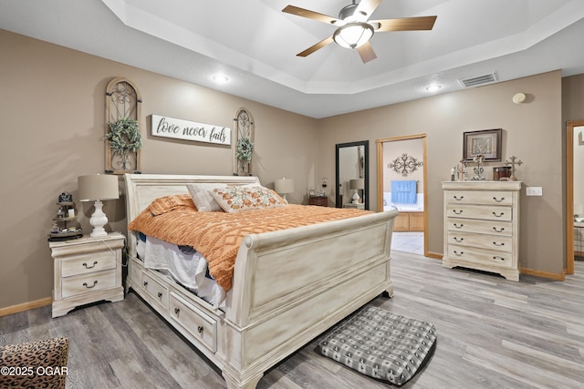 bedroom with ensuite bath, wood-type flooring, and a tray ceiling