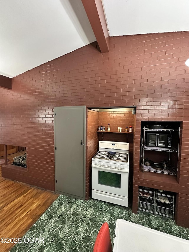 kitchen with brick wall, wood-type flooring, white gas stove, and vaulted ceiling with beams