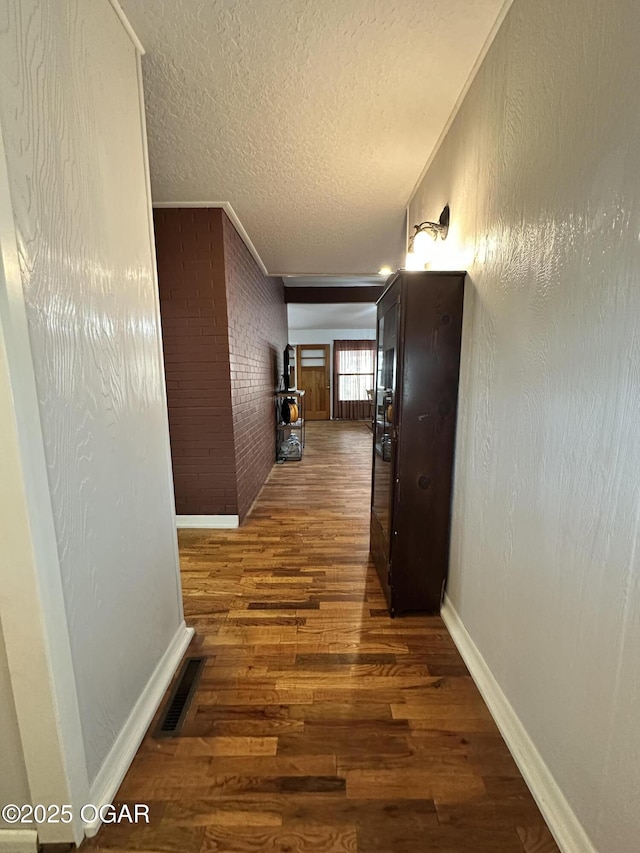 hall with brick wall, dark hardwood / wood-style floors, and a textured ceiling