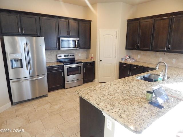 kitchen with light stone counters, sink, dark brown cabinets, and appliances with stainless steel finishes