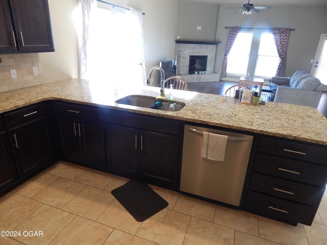 kitchen featuring sink, light stone counters, a brick fireplace, stainless steel dishwasher, and decorative backsplash