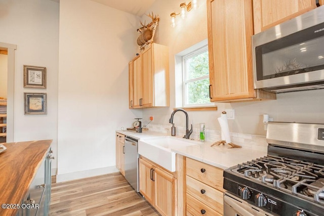 kitchen featuring appliances with stainless steel finishes, sink, butcher block counters, light brown cabinets, and light wood-type flooring