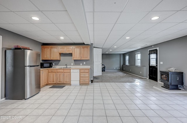 kitchen featuring light brown cabinetry, sink, a wood stove, stainless steel fridge, and white dishwasher