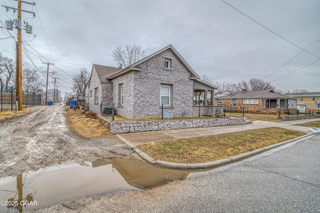 view of property exterior with a shingled roof, stone siding, fence, and central AC unit