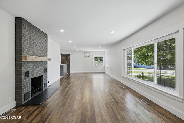 540 E 4th St, Baxter Springs, KS 66713 - unfurnished living room with a barn door, dark wood-type flooring, baseboards, recessed lighting, and a brick fireplace
