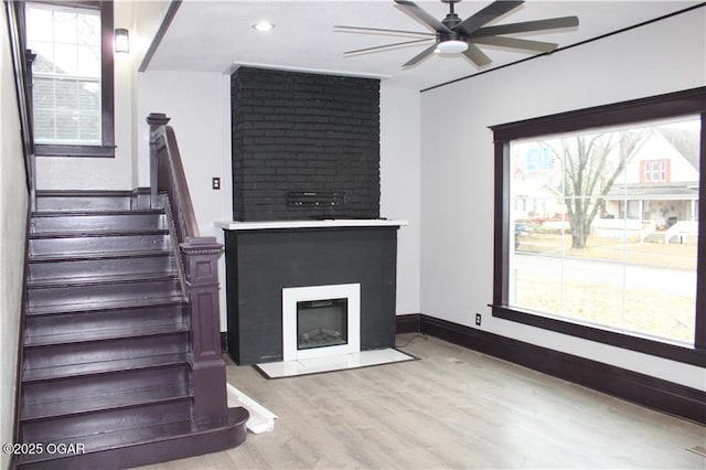 unfurnished living room featuring a healthy amount of sunlight, a large fireplace, ceiling fan, and light wood-type flooring