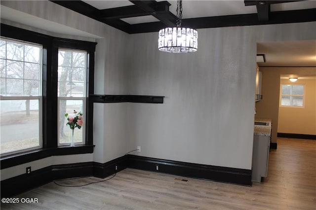 unfurnished dining area with beamed ceiling, coffered ceiling, and light hardwood / wood-style floors