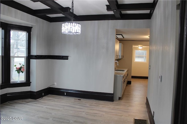 unfurnished dining area with beamed ceiling, coffered ceiling, sink, and light hardwood / wood-style floors