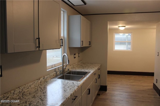 kitchen with white cabinetry, light hardwood / wood-style floors, sink, and light stone counters