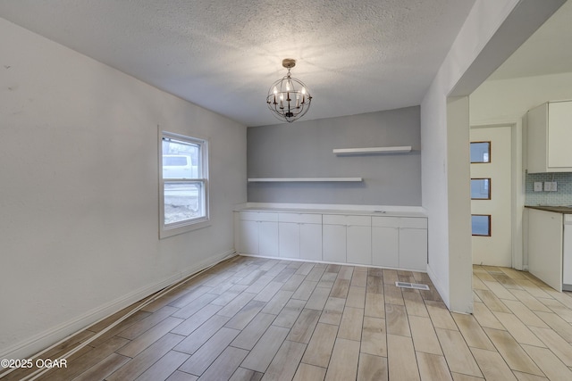 unfurnished dining area featuring light wood-type flooring, a textured ceiling, and a chandelier