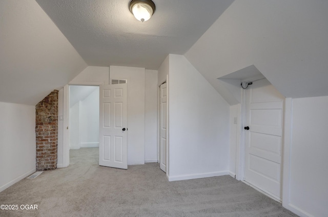 additional living space with vaulted ceiling, light carpet, and a textured ceiling