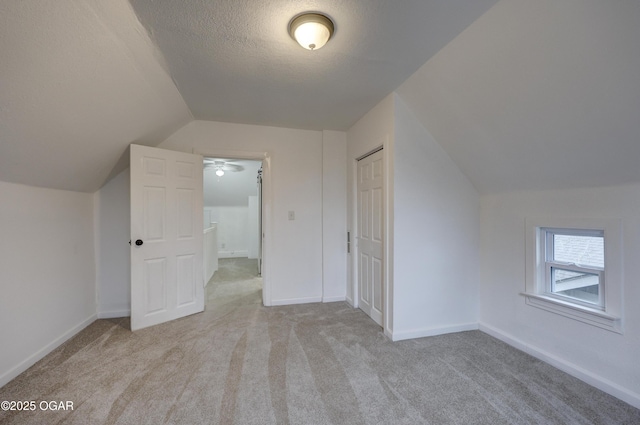 additional living space with light colored carpet, lofted ceiling, and a textured ceiling