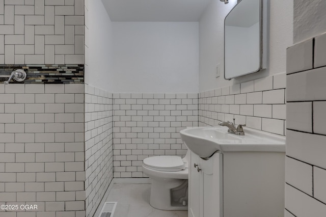 bathroom with vanity, toilet, and tile walls