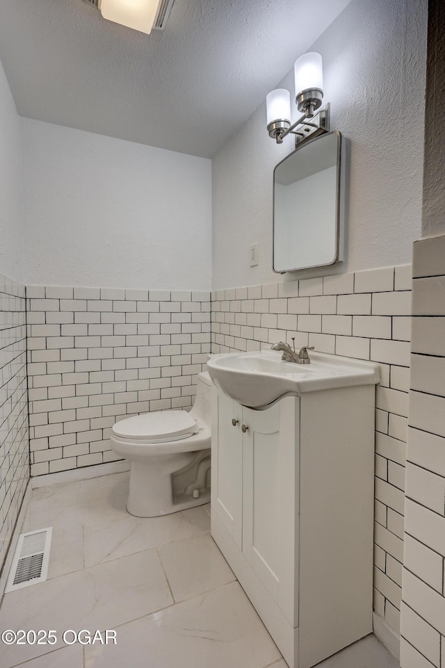 bathroom featuring vanity, tile walls, a textured ceiling, and toilet